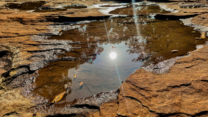 A serene puddle reflecting the bright sun amidst rugged brown rocks, conveying a concept of natural tranquility and the simplicity of earth's beauty