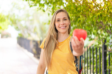 Young blonde woman with an apple at outdoors with happy expression