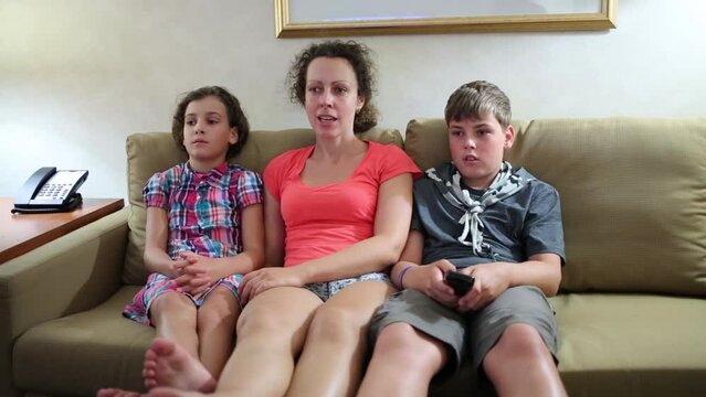 Woman with two children sit on couch and watch tv at home