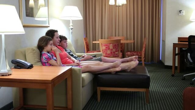 Barefoot woman with two children sit on couch and watch tv in room