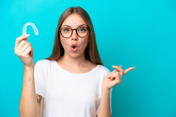 Young Lithuanian woman holding invisible braces isolated on blue background surprised and pointing...
