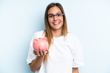 Young caucasian woman holding a piggybank isolated on blue background with surprise and shocked...