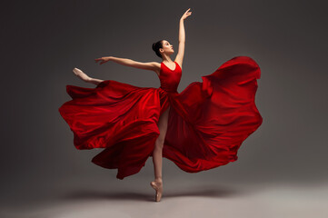 Ballerina. Young graceful woman ballet dancer, dressed in professional outfit, shoes and red weightless skirt is demonstrating dancing skill. Beauty of classic ballet. - 714633598