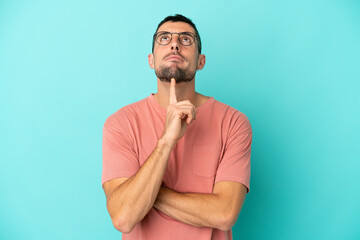 Young handsome caucasian man isolated on blue background With glasses and looking up