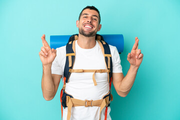 Young mountaineer caucasian man with a big backpack isolated on blue background with fingers...