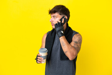 Young sport caucasian man with towel isolated on yellow background holding coffee to take away and...