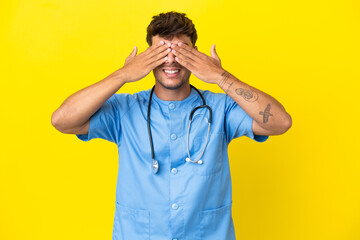 Young surgeon doctor man isolated on yellow background covering eyes by hands