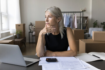 Thoughtful serious businesswoman sit at desk with laptop, heap of invoices and bills, thinking of bad sales month results, deep in thoughts, search financial problem solution, accounting, bankruptcy