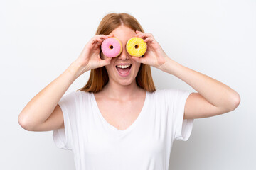 Young redhead woman isolated on white background holding donuts in an eye
