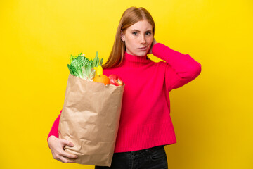 Young redhead woman holding a grocery shopping bag isolated on yellow background having doubts