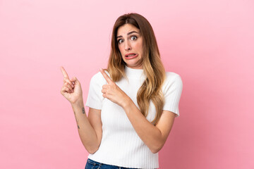 Caucasian woman isolated on pink background frightened and pointing to the side