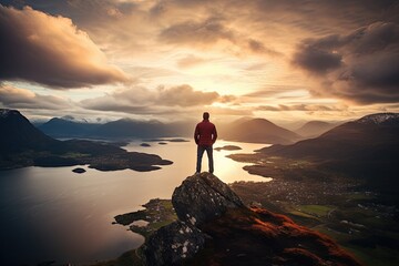 Explorer stands on a rocky outcrop, gazing into the distance as the setting sun casts a warm glow over a serene fjord and rugged mountains.