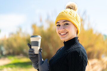 Young moroccan girl wearing winter muffs while holding a coffee at outdoors and pointing it