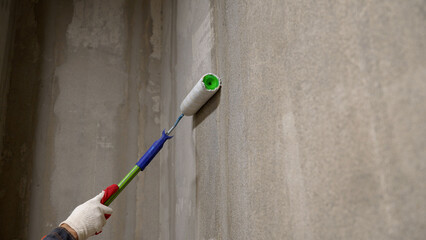 A worker primes walls in a new building. Roller brush with primer for plastering walls. Concept of...