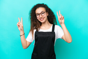 Restaurant waiter Arab woman isolated on blue background showing victory sign with both hands