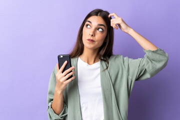 Naklejka premium Young caucasian woman using mobile phone isolated on purple background having doubts and with confuse face expression