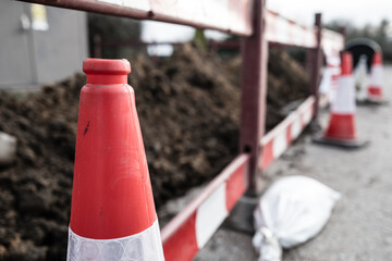 Shallow focus of a standard British traffic cone seen at the edge of a roadworks barrier. The soil...