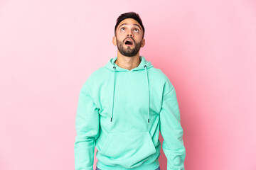 Young caucasian man isolated on pink background looking up and with surprised expression