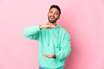 Young caucasian man isolated on pink background holding copyspace imaginary on the palm to insert an ad