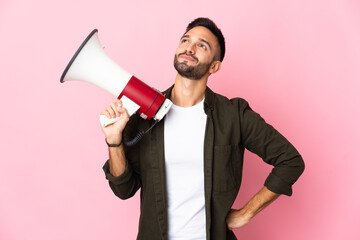 Young caucasian man isolated on pink background holding a megaphone and thinking