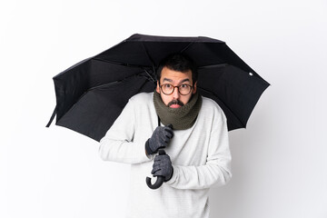 Caucasian handsome man with beard holding an umbrella over isolated white wall