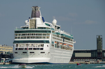 Luxury cruise ship Rhapsody with tug boats at the cruise terminal in the port of Venice Venezia with skyline and traffic on waterway