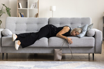 Full-length view tired mature woman felt asleep on sofa, arrive at home after party or hard-working...
