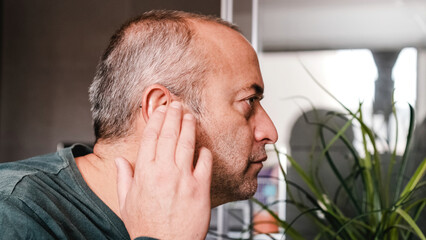 Obraz premium Adult man putting his hearing aids in his ears at home