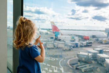 Cute little toddler girl at the airport, traveling. Happy healthy child waiting near window and...