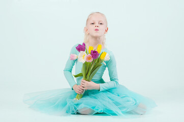 A beautiful tender girl with long curly blond hair holds a bouquet of tulips in her hands. Blue background