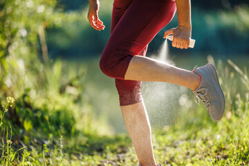 Woman spraying insect repellent against mosquito and tick on her leg before jogging in nature