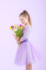 A beautiful tender girl in a purple fluffy skirt holds a bouquet of tulips in her hands. Purple background