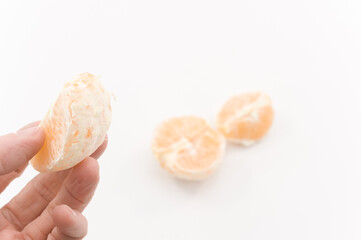 mmano che regge spicchio di frutto di arancia sbucciato, superficie bianca 