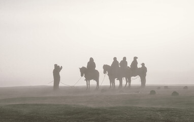 Silhouettes of riders on horseback in the fog