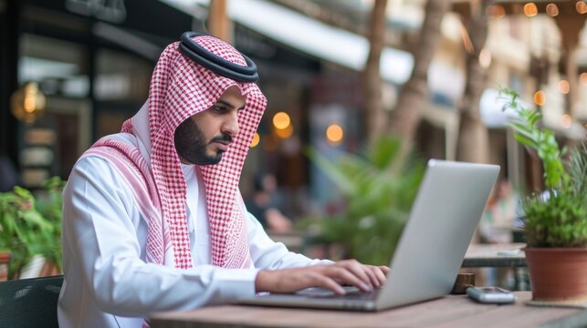 Saudi Arab business man on laptop working outdoor wearing traditional dress. Muslim businessman from Saudi Arabia typing