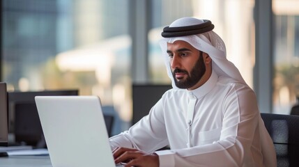 Successful Arab Businessman in White Traditional Outfit Sitting in Office and Working on Laptop Computer. Business Manager Planning Corporate Strategy. Saudi, Emirati, Arab Businessman Concept. 
