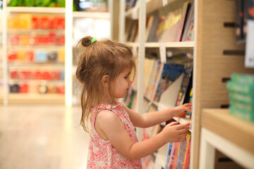 Fototapeta na wymiar Little cute child picking books from the bookshelf
