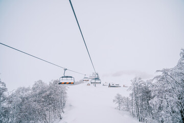 Fototapeta na wymiar Chair lift climbs up a snowy mountain with small houses