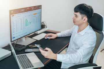 Handsome young businessman is trading the stock market via computer and smartphone.