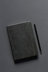 Blank black notepad and black pencil on a dark background. Monochrome photo. Business concept. Copy space for your text.