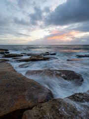 Cloudy sunrise view over a rocky coastline.