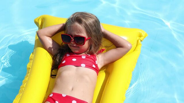 Cute little girl lying on inflatable mattress in swimming pool with blue water on warm summer day on tropical vacations. Summertime activities concept. Cute little girl sunbathing on air mattress