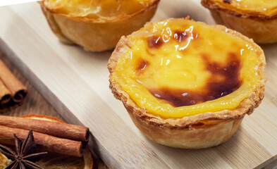 Three Pastel de nata or Portuguese egg tart and cinnamon sticks on a wooden brown background. Pastel de Belm is a small dessert, a cup-shaped pastry made from puff pastry with custard.