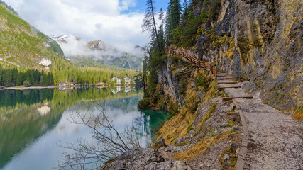 Fototapeta na wymiar panoramic landscape of mountain lake Braies in the Dolomites, Italy. Hiking trail along the lake and low clouds over the mountain