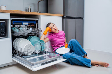 Young woman sitting on the floor near the dishwasher machine