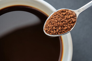 Close up of Instant Coffee on Stainless Steel Tea Spoon with Black Coffee in White Cup, Black Background.