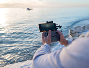 the remote control from the drone is in the hands of a man and the quadcopter is in flight against the background of the sea