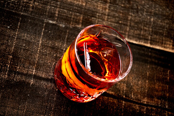 glass of red negroni drink with orange slices and clear ice block on wooden table