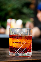 glass of red negroni cocktail with orange slices and clear ice block on wooden table blurred table background
