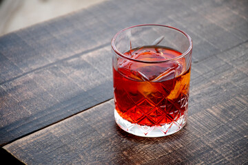 glass of red negroni cocktail with orange slices and clear ice block on wooden table